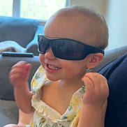 Kleo is registered to the contest to win money with this photo: child, toddler, baby, sunglasses, smiling, happy, laughing, portrait, indoor, couch, window, sunlight, floral_outfit, lemon_pattern, fashion, sitting, raised_fists, arms, home, photography