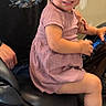 toddler, child, girl, smiling, sitting, motorcycle, vehicle, indoor, portrait, person, adult, graphic_tshirt, pink_dress, blonde_hair, face, hands, handlebars, candid, home, happy