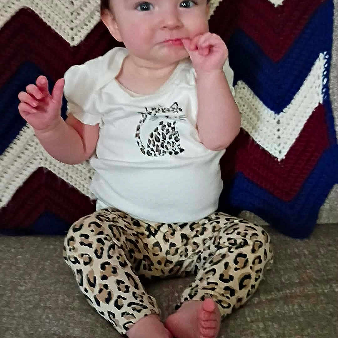 Isabel joined the competition — help win amazing prizes! baby, infant, child, sitting, couch, blanket, zigzag_pattern, leopard_print, clothing, cute, face, hands, feet, indoor, portrait, person, expression, curious, young, casual
