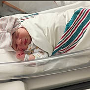 Isabel joined the competition — help win amazing prizes! newborn, baby, sleeping, hospital, bassinet, blanket, bow, hat, swaddled, infant, child, cute, resting, face, bed, healthcare, person, soft, cozy, small