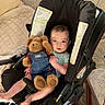 baby, blanket, car_seat, child, clothing, comfort, cushion, face, footwear, furniture, home, indoor, infant, legs, person, plush_toy, portrait, seated, smile, teddy_bear