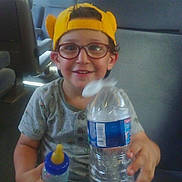 Djilani participe au concours pour gagner de l'argent avec cette photo : baby_bottle, bottle, boy, bus_seat, casual_clothing, child, daylight, glasses, happy, holding, indoor, portrait, seat, sitting, smiling, transportation, water_bottle, window, yellow_cap, young_child