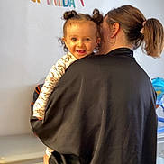 Manël a rejoint le concours — aidez-le/la à gagner de superbes lots ! toddler, child, adult, birthday, celebration, indoor, hair_buns, smiling, person, clothing, banner, cabinet, earrings, pony_tail, holding, face, happy, home, curly_hair, curtain