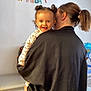 toddler, child, adult, birthday, celebration, indoor, hair_buns, smiling, person, clothing, banner, cabinet, earrings, pony_tail, holding, face, happy, home, curly_hair, curtain