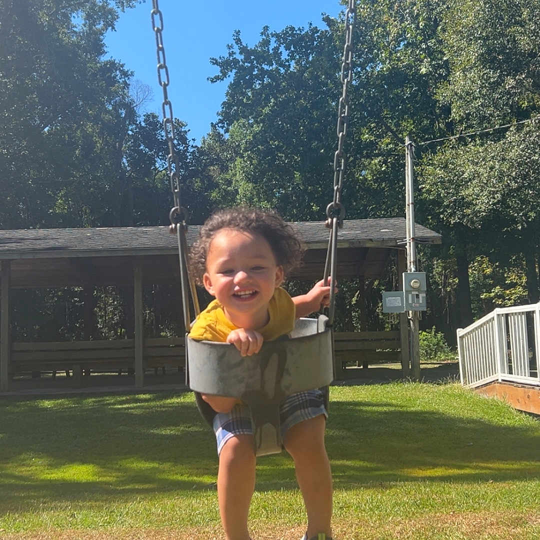 Kyzer is registered to the contest to win money with this photo: casual_clothing, child, daytime, fun, grass, happy, joy, motion, nature, outdoor, park, playground, recreation, shorts, smiling, sneakers, sunny, swing, toddler, trees