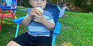 Kyzer is registered to the contest to win money with this photo: child, toddler, outdoor, grass, trees, cupcake, food, chair, blue_chair, picnic, play, summer, nature, barefoot, grass_field, smiling, people, kids, fun, daytime