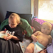 Louis is registered to the contest to win money with this photo: baby, child, diaper, container, cereal, bed, blanket, pillow, window, sunlight, indoor, person, relaxing, casual, family, young_child, clothing, purple, green, black_shirt