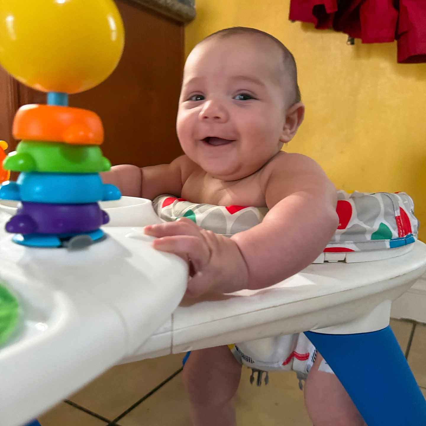 Leon joined the competition — help win amazing prizes! baby, walker, toy, smile, indoor, happy, child, colorful, playtime, legs, hand, face, kitchen, floor, clothing, infant, furniture, person, background, red_cloth