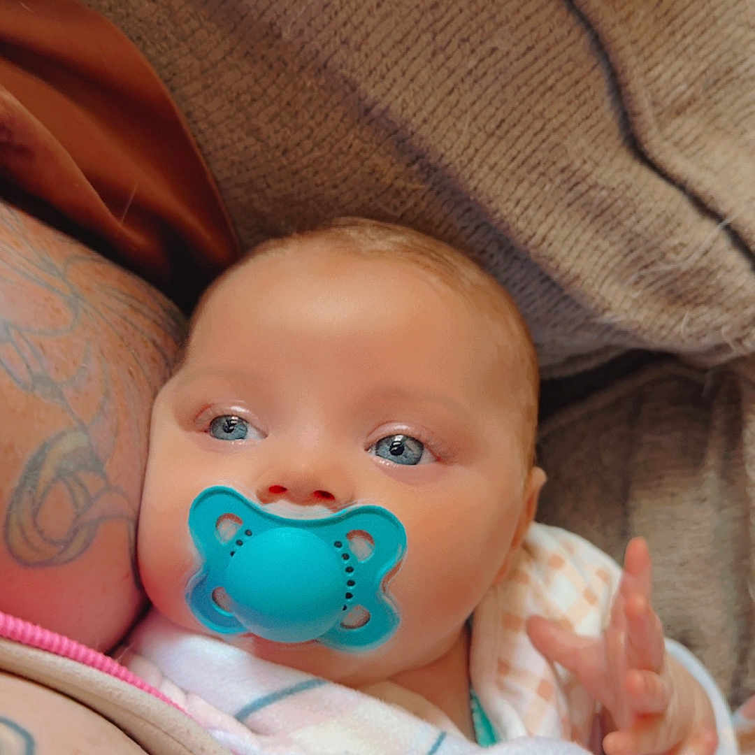 Malina is registered to the contest to win money with this photo: arm, baby, blanket, blue_eyes, closeup, comfort, couch, cozy, hand, indoor, infant, newborn, pacifier, peaceful, person, portrait, resting, skin, soft_texture, tattoo