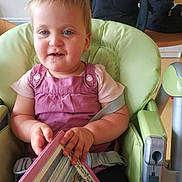 Melyo a rejoint le concours — aidez-le/la à gagner de superbes lots ! toddler, child, high_chair, book, reading, pink_clothing, blue_eyes, indoor, kitchen, baby, seatbelt, furniture, person, portrait, cute, holding, smiling, young_child, domestic, home