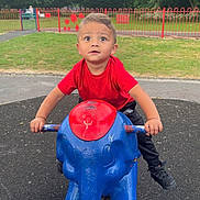 Amarni joined the competition — help win amazing prizes! blue_elephant, casual_clothing, child, curious, daylight, elephant, expression, fence, footwear, grass, outdoor, park, play, playground, red_shirt, rocker, toddler, toy, trees, young_child
