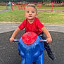 blue_elephant, casual_clothing, child, curious, daylight, elephant, expression, fence, footwear, grass, outdoor, park, play, playground, red_shirt, rocker, toddler, toy, trees, young_child