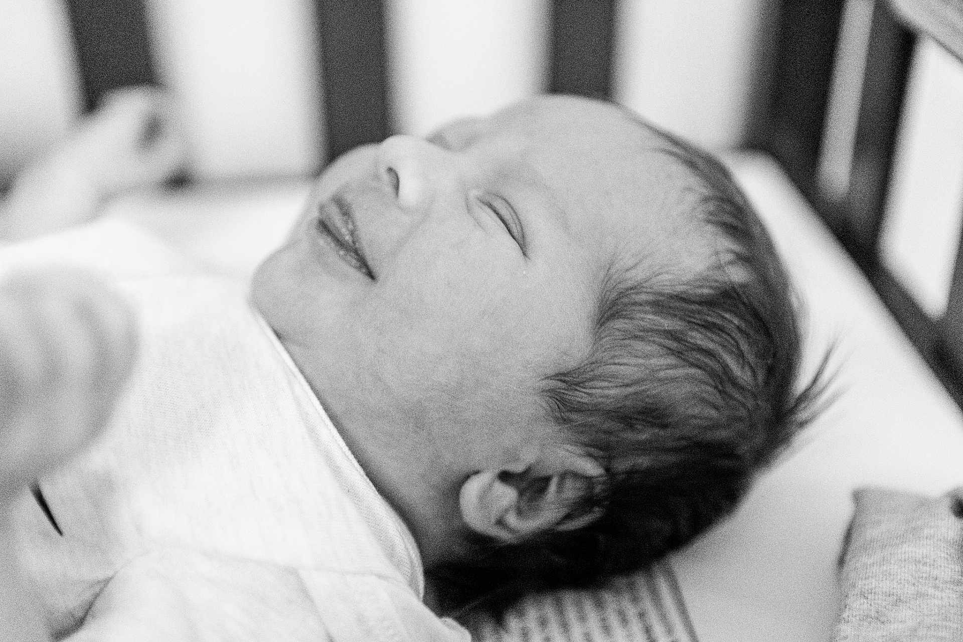 Luca joined the competition — help win amazing prizes! newborn, baby, infant, sleeping, smiling, black_and_white, portrait, close_up, face, head, hair, crib, blanket, soft_focus, peaceful, resting, cute, indoors, person, child
