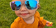 Realynn is registered to the contest to win money with this photo: cheese_puffs, child, cute, event, face, fashion, fun, grass, hand, orange_clothing, outdoor, people, playful, portrait, reflection, smile, snack, sunglasses, sunlight, toddler