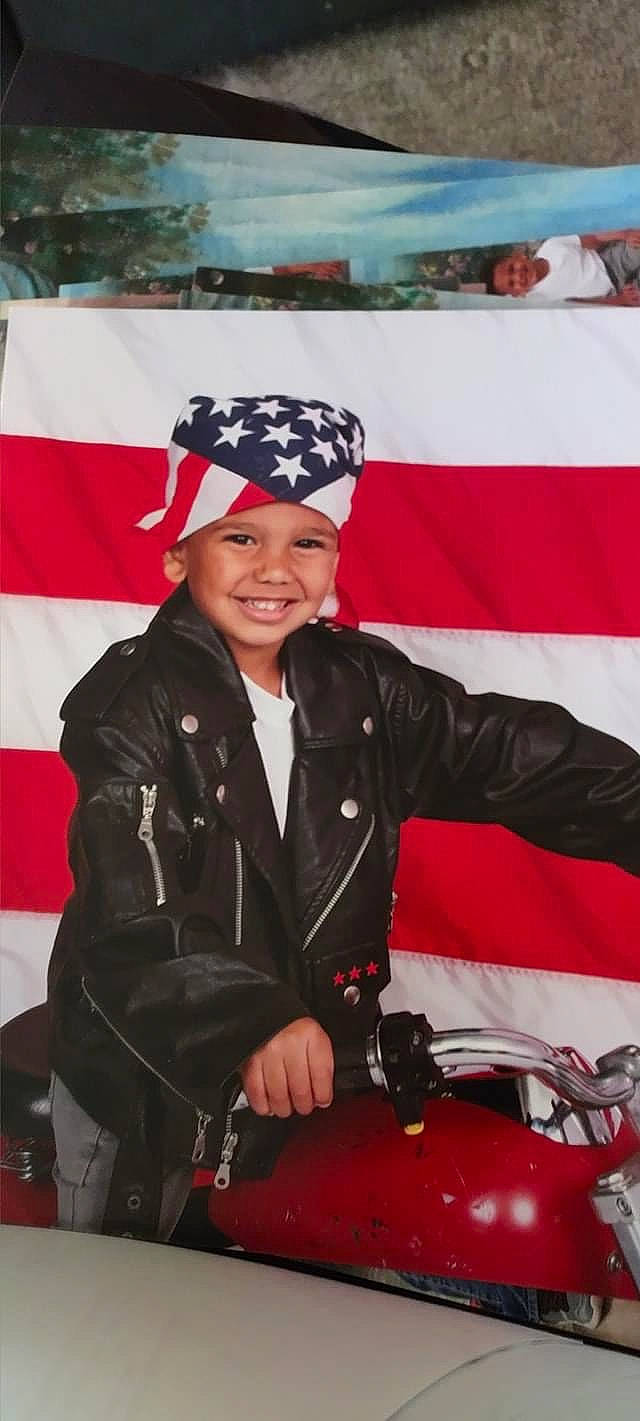 Bradley is registered to the contest to win money with this photo: automotive_lighting, blurred, cap, coat, event, gesture, glove, headgear, headwear, jacket, joy, leather_jacket, military_uniform, motor_vehicle, motorcycle, official, person, personal_protective_equipment, smile, snapshot