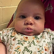 Kaliyah joined the competition — help win amazing prizes! baby, infant, child, face, eyes, drooling, bubbles, onesie, floral_pattern, close_up, portrait, caregiver, lap, blanket, wall, brick_wall, indoor, sitting, expression, gaze