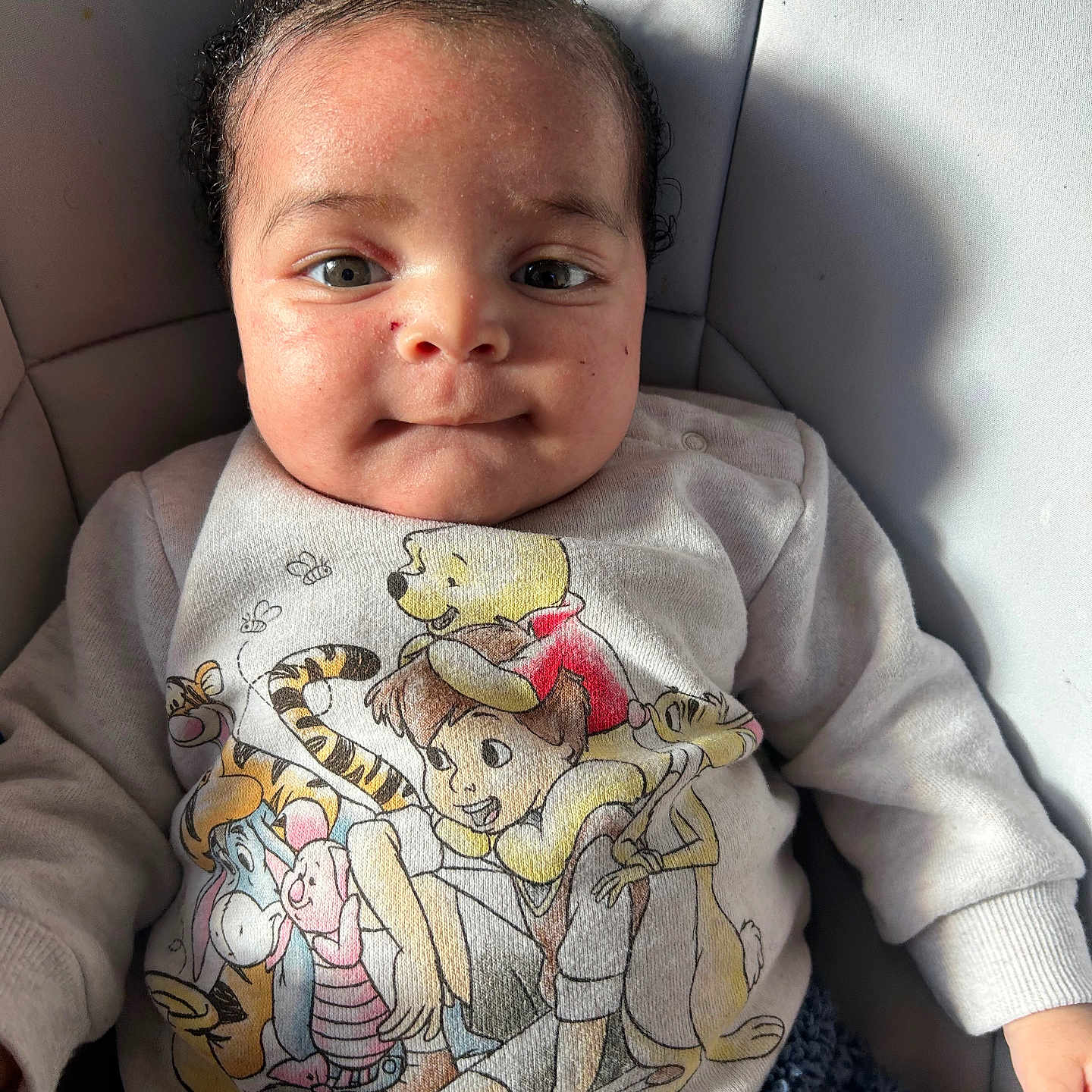 Lucksson is registered to the contest to win money with this photo: baby, cartoon_print, chair, closeup, cozy_clothing, curly_hair, eyes, face, fingers, hand, infant, onesie, portrait, seat, shadow, skin, smile, soft_light, sweater, winnie_the_pooh