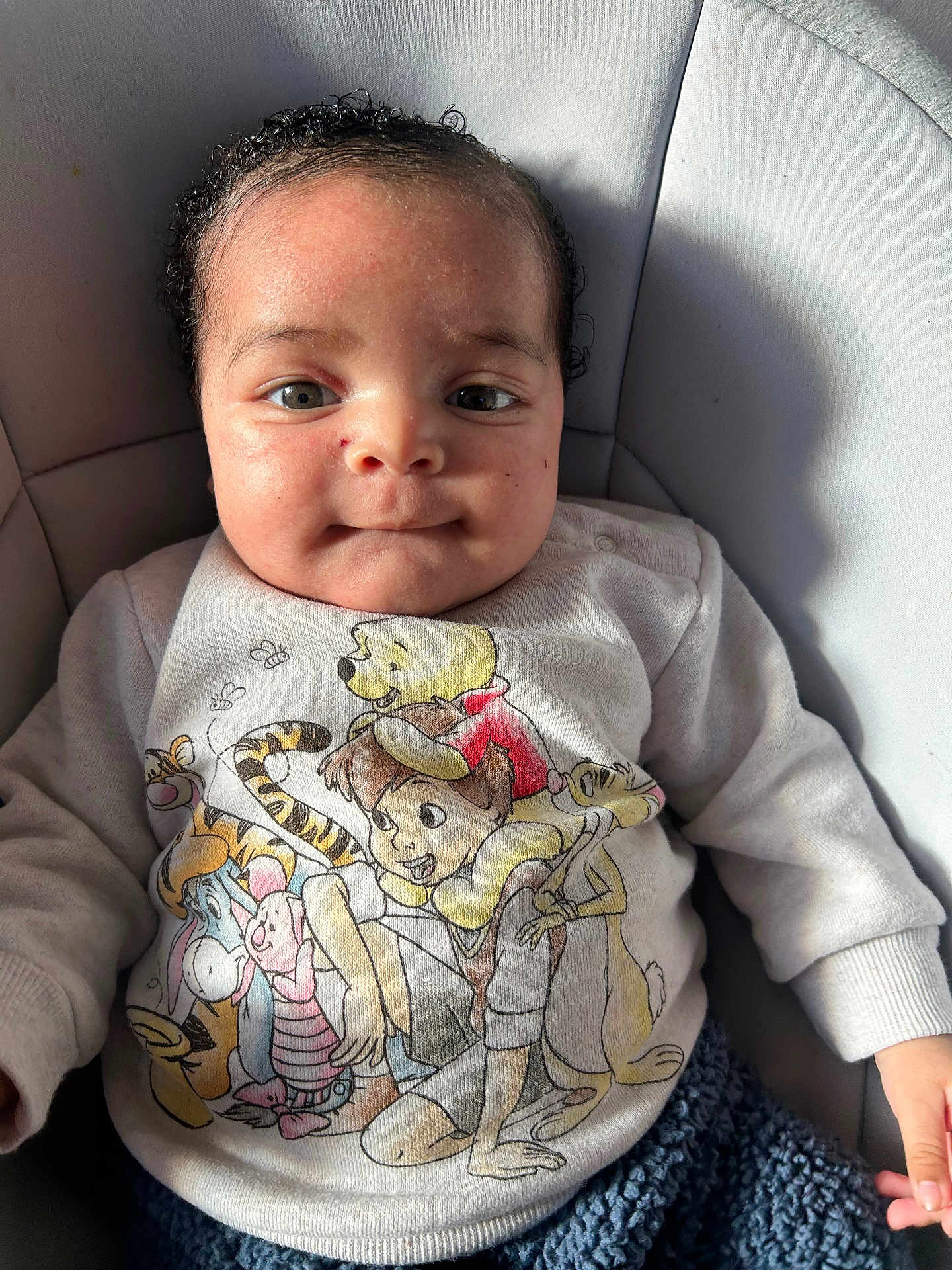 Lucksson is registered to the contest to win money with this photo: baby, infant, face, eyes, smile, curly_hair, winnie_the_pooh, sweater, cartoon_print, onesie, seat, chair, closeup, portrait, skin, hand, fingers, soft_light, shadow, cozy_clothing