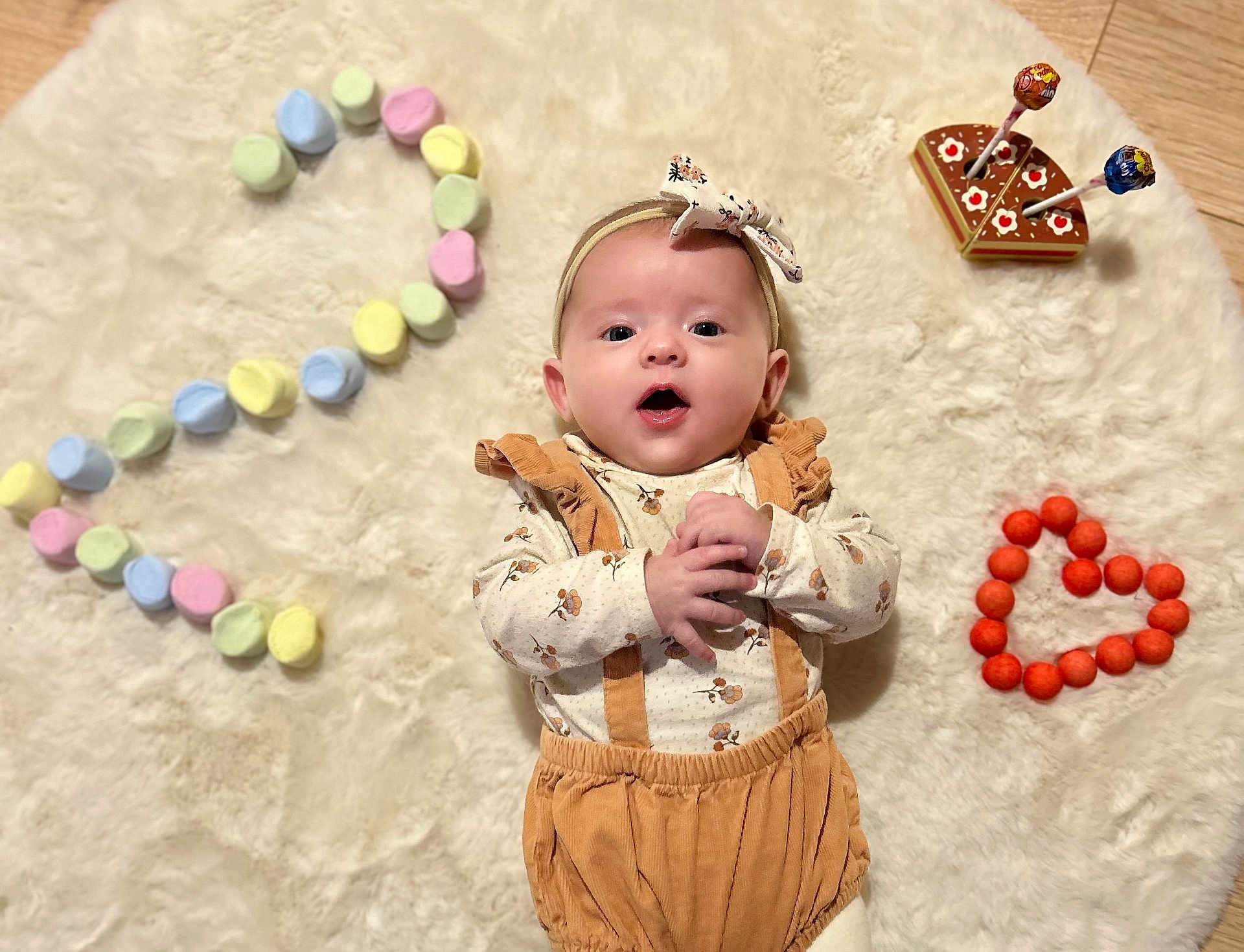 Amaya participe au concours pour gagner de l'argent avec cette photo : baby, infant, headband, marshmallows, number_two, heart_shape, orange_balls, cake_toy, lollipops, soft_rug, wooden_floor, clothing, suspenders, cute, lying_down, indoors, portrait, child, celebration, playful