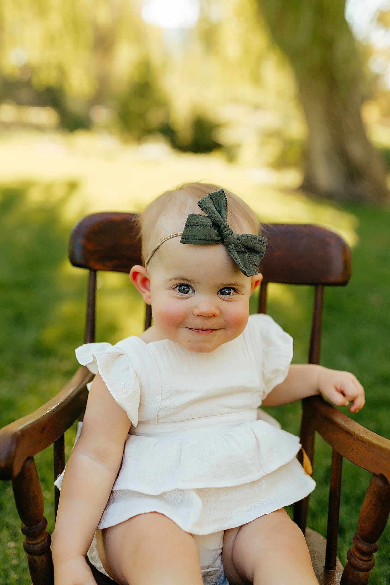 Poppy joined the competition — help win amazing prizes! baby, child, smile, headband, green_bow, white_dress, wooden_chair, outdoor, grass, daylight, portrait, cute, infant, young_child, face, happy, sitting, nature, sunlight, blurry_background