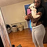 Snoopy is registered to the contest to win money with this photo: woman, dog, mirror, selfie, phone, wooden_floor, laundry_basket, clothing, home_interior, casual, black_hair, pet, affection, barefoot, long_pants, short_sleeve, pink_phone, reflection, indoor, furniture