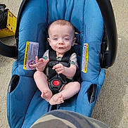 Niklaus joined the competition — help win amazing prizes! baby, background_objects, blue, camera_angle, camo_pattern, car_seat, casual_clothing, child, concrete, cute, daylight, expression, footwear_absent, hand_gesture, infant, outdoor, person, safety_harness, seat, strapped