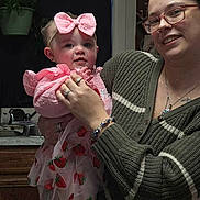 Ellie joined the competition — help win amazing prizes! baby, child, woman, glasses, pink_bow, strawberry_dress, kitchen, holding, smile, person, indoor, sweater, rings, bracelet, marble_countertop, sink, plant, cabinet, portrait, family