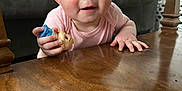 Octavia is registered to the contest to win money with this photo: baby, infant, child, toy, figurine, wooden_table, coffee_table, living_room, sofa, crawling, pink_clothing, blue_eyes, hand, cheeks, portrait, close_up, furniture, wood_texture, curious, smile