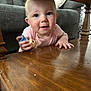 baby, infant, child, toy, figurine, wooden_table, coffee_table, living_room, sofa, crawling, pink_clothing, blue_eyes, hand, cheeks, portrait, close_up, furniture, wood_texture, curious, smile