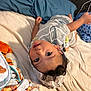 child, baby, bed, blanket, pillow, clothing, hoodie, cartoon, face, smile, indoor, person, cute, cozy, fabric, soft, playful, curly_hair, toddler, resting
