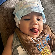 Xavier joined the competition — help win amazing prizes! baby, child, diaper, bib, tongue_out, playful, smiling, face, headwear, clothing, infant, cute, expression, lying_down, fabric, texture, casual, indoors, closeup, happy
