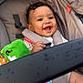 Xavier is registered to the contest to win money with this photo: baby, smiling, stroller, child, curly_hair, toy, harness, seat, colorful, fabric, happy, infant, cute, closeup, portrait, child_seat, playful, bright, cheerful, safety