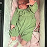 baby, infant, green_outfit, blanket, bassinet, soft_texture, white_socks, hand, face, cute, newborn, cozy, lying_down, pink_blanket, clothing, person, indoor, sleeping_area, child, portrait