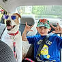 Diesel is registered to the contest to win money with this photo: dog, sunglasses, boy, cap, minions, tshirt, seatbelt, car_interior, backseat, leash, hand_gesture, smile, sunlight, window, happy, pet, child, playful, friendship, casual
