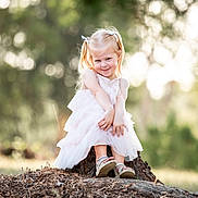 Hazel is registered to the contest to win money with this photo: child, girl, dress, outdoor, nature, tree_stump, smile, sunlight, forest, blurry_background, happy, cute, portrait, sitting, young, shoes, pigtails, playful, daylight, grass
