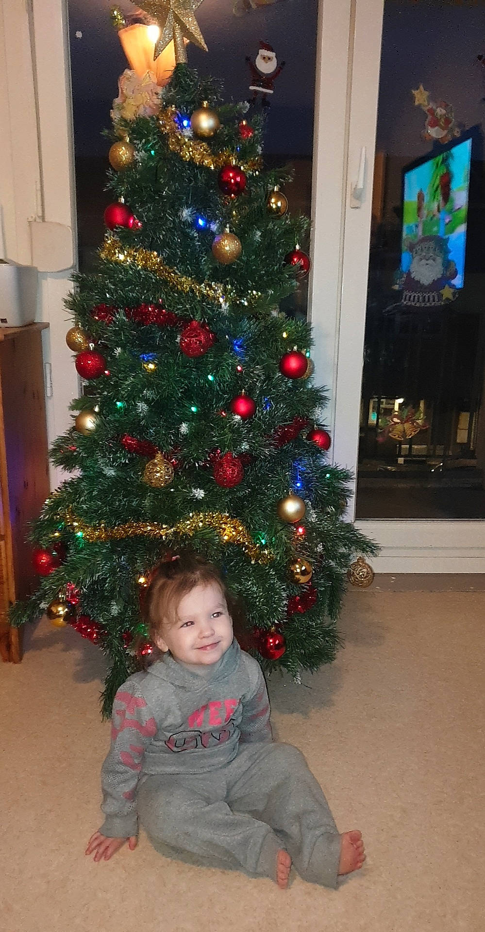 Stella participe au concours pour gagner de l'argent avec cette photo : christmas_decoration, christmas_ornament, christmas_tree, conifer, event, evergreen, holiday, holiday_ornament, joy, larch, ornament, person, photograph, plant, smile, standing, tints_and_shades, toddler, tree, white