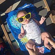 Ezekiel joined the competition — help win amazing prizes! baby, infant, sunglasses, yellow_sunglasses, towel, beach_towel, lounge_chair, onesie, stars_pattern, hands, legs, feet, outdoor, sunny, shadow, paved_floor, tiles, relaxing, playful, family