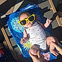 baby, infant, sunglasses, yellow_sunglasses, towel, beach_towel, lounge_chair, onesie, stars_pattern, hands, legs, feet, outdoor, sunny, shadow, paved_floor, tiles, relaxing, playful, family