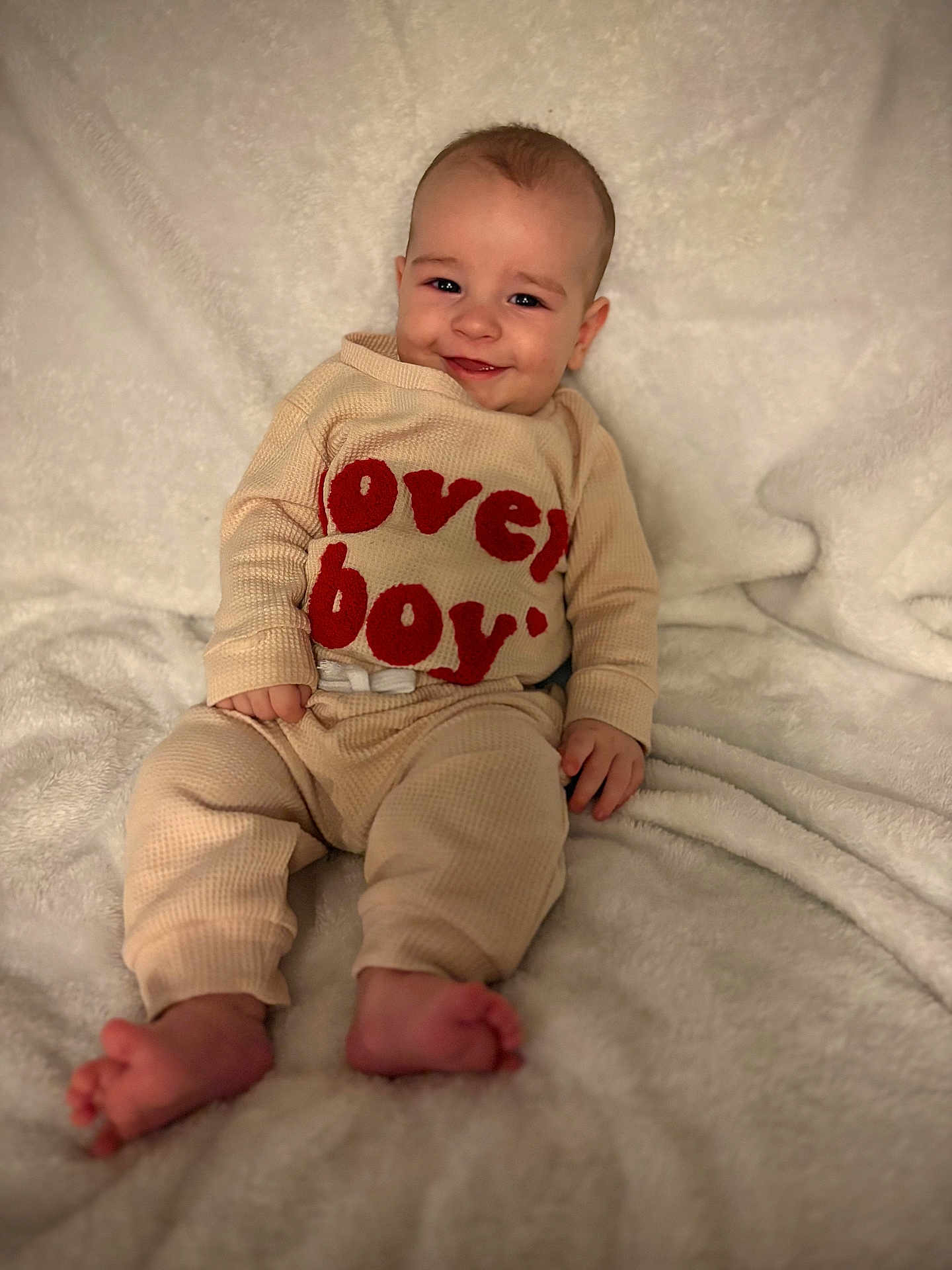 Dayton Jr joined the competition — help win amazing prizes! baby, infant, smiling, blanket, sweater, text_on_clothing, cute, portrait, indoor, cozy, soft_texture, lying_down, feet, hands, eyes, cheeks, skin, bokeh, photography, happy