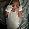 baby, infant, white_onesie, mittens, lying_down, blanket, texture, furrowed_brow, curious, person, face, headwear, indoors, soft_lighting, closeup, newborn, skin, expression, sleepwear, cozy