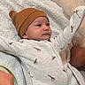 baby, infant, child, portrait, lying_down, smiling, wide_eyes, hat, beanie, onesie, giraffe_pattern, blanket, bed, bedding, pillow, indoor, cozy, cute, arms_raised, closeup