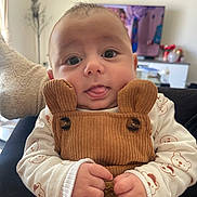 Milan participe au concours pour gagner de l'argent avec cette photo : baby, infant, child, cute, tongue_out, brown_overall, corduroy, bear_ears, white_shirt, bear_prints, hands, indoor, living_room, television, home_decor, portrait, close_up, playful, curious_eyes, seated