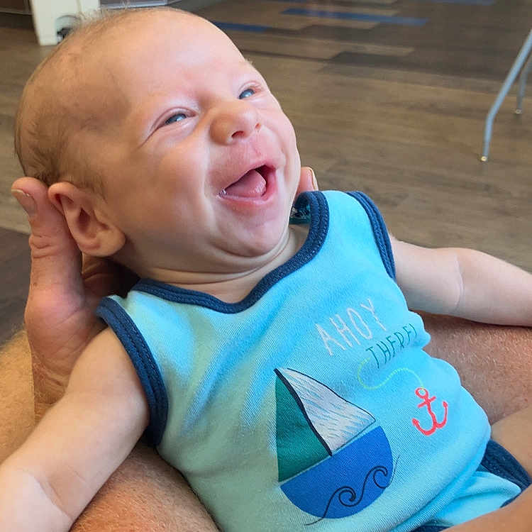Nikolai Berry joined the competition — help win amazing prizes! adult, arm, baby, background, blue_onesie, casual_clothing, child, counter, floor, furniture, happy, holding, human, indoor, infant, laughing, person, sailboat, skin, smiling