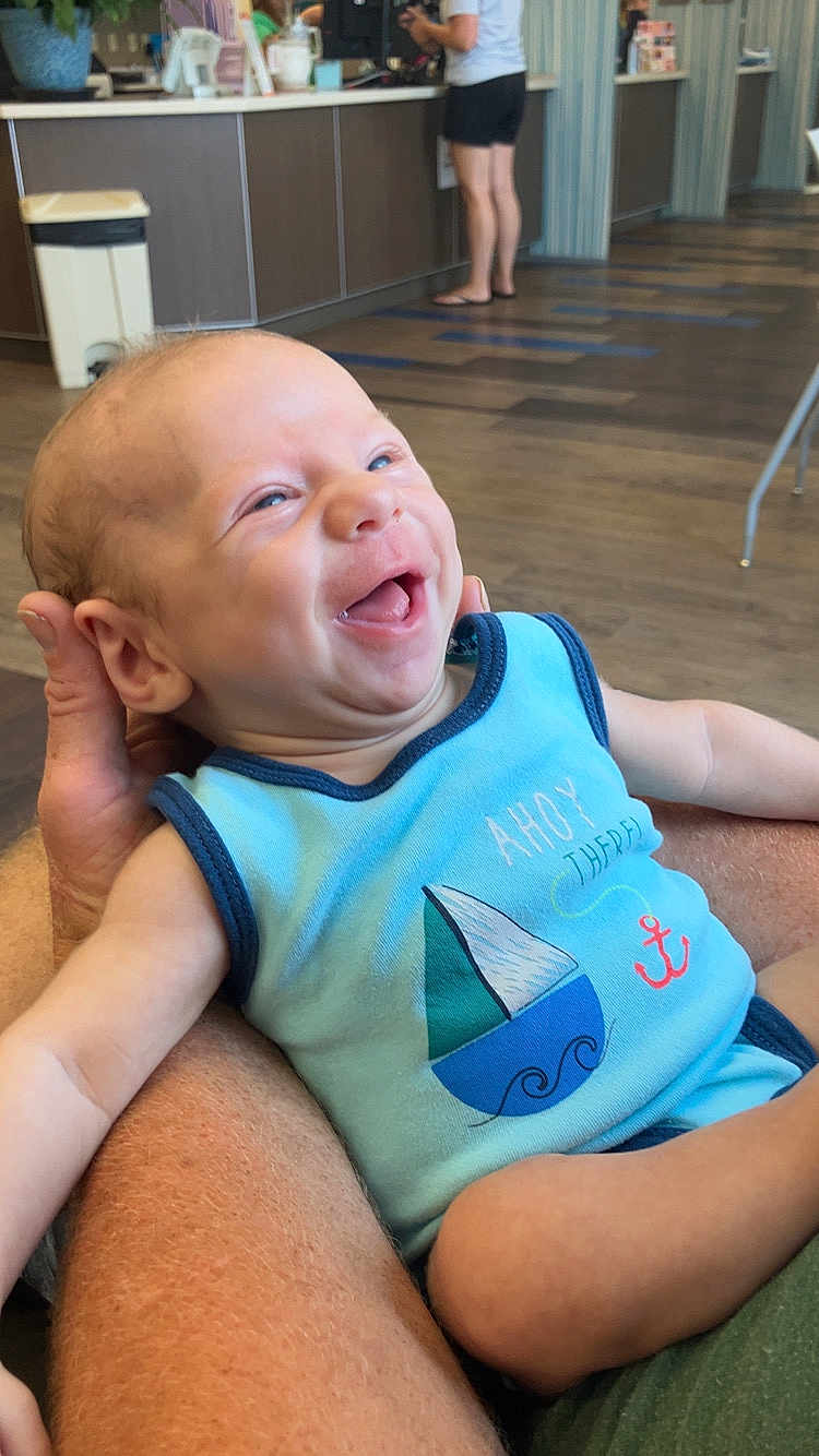 Nikolai Berry joined the competition — help win amazing prizes! baby, child, infant, smiling, happy, blue_onesie, sailboat, arm, person, indoor, floor, counter, casual_clothing, holding, laughing, skin, human, background, adult, furniture