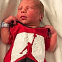 Nikolai Berry is registered to the contest to win money with this photo: baby, newborn, infant, red_onesie, jordan_logo, clothing, blanket, sleeping, person, skin, hand, face, head, cute, soft, indoors, portrait, resting, newborn_baby, baby_clothes