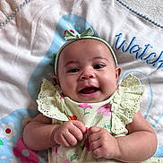 Ivy is registered to the contest to win money with this photo: baby, smiling, infant, headband, bow, floral_dress, hands, blanket, pattern, colorful, happy, cute, lying_down, young_child, soft_texture, indoors, portrait, face, skin, child