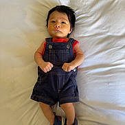 Gabriel is registered to the contest to win money with this photo: baby, infant, denim_overalls, red_shirt, blue_shoes, lying_down, blanket, indoor, cute, serious_expression, clothing, footwear, small_hands, portrait, child, young, soft_lighting, casual_wear, fashion, newborn