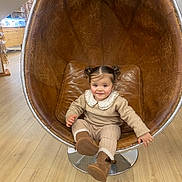 Naila participe au concours pour gagner de l'argent avec cette photo : child, toddler, girl, face, pigtails, smile, chair, egg_chair, leather, boots, outfit, collar, sitting, indoor, wooden_floor, store, retail_display, hand, cozy, playful
