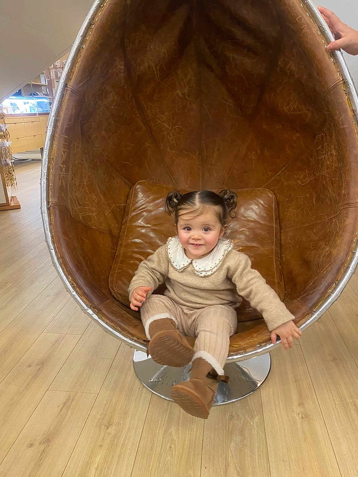 Naila participe au concours pour gagner de l'argent avec cette photo : child, toddler, girl, face, pigtails, smile, chair, egg_chair, leather, boots, outfit, collar, sitting, indoor, wooden_floor, store, retail_display, hand, cozy, playful