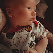 Felix joined the competition — help win amazing prizes! baby, infant, child, portrait, close_up, indoors, blanket, onesie, superhero, clothing, sitting, lying_down, calm, serious_expression, face, hand, arm, tattoo, warm_lighting, cozy